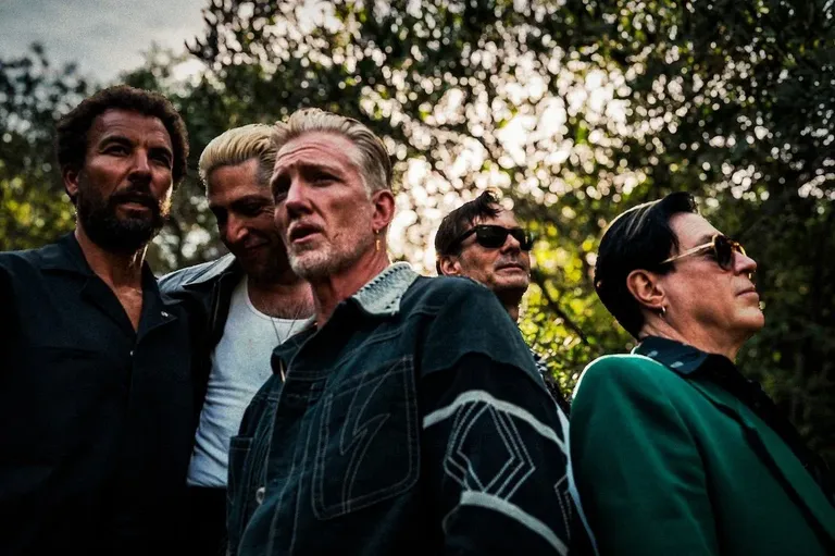 Rock band Queens of the Stone Age posing outdoors by Andreas Neumann, featuring Josh Homme and band members against a backdrop of trees.